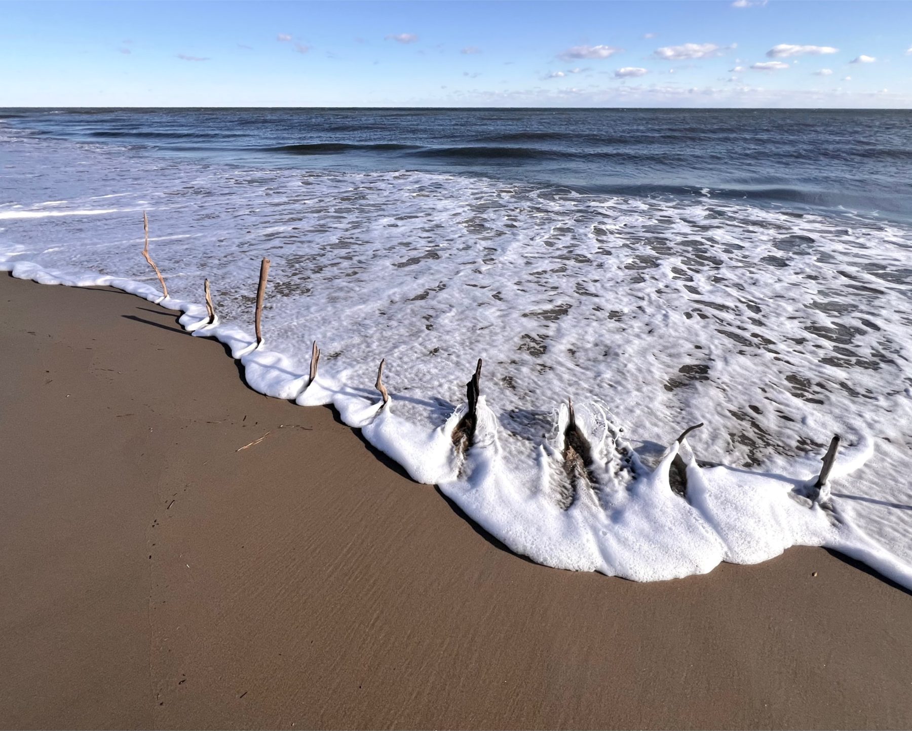 Sticks planted in the sand as a wave washes in