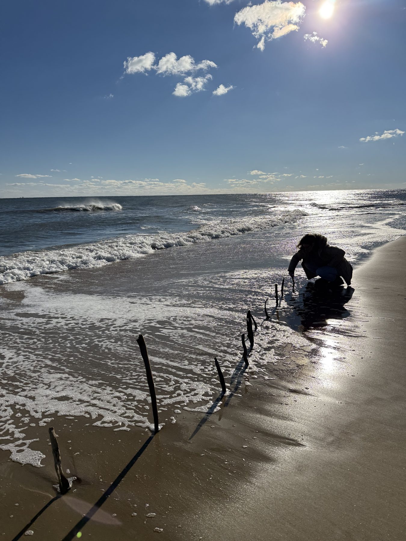 The artist kneeling at the shoreline placing sticks