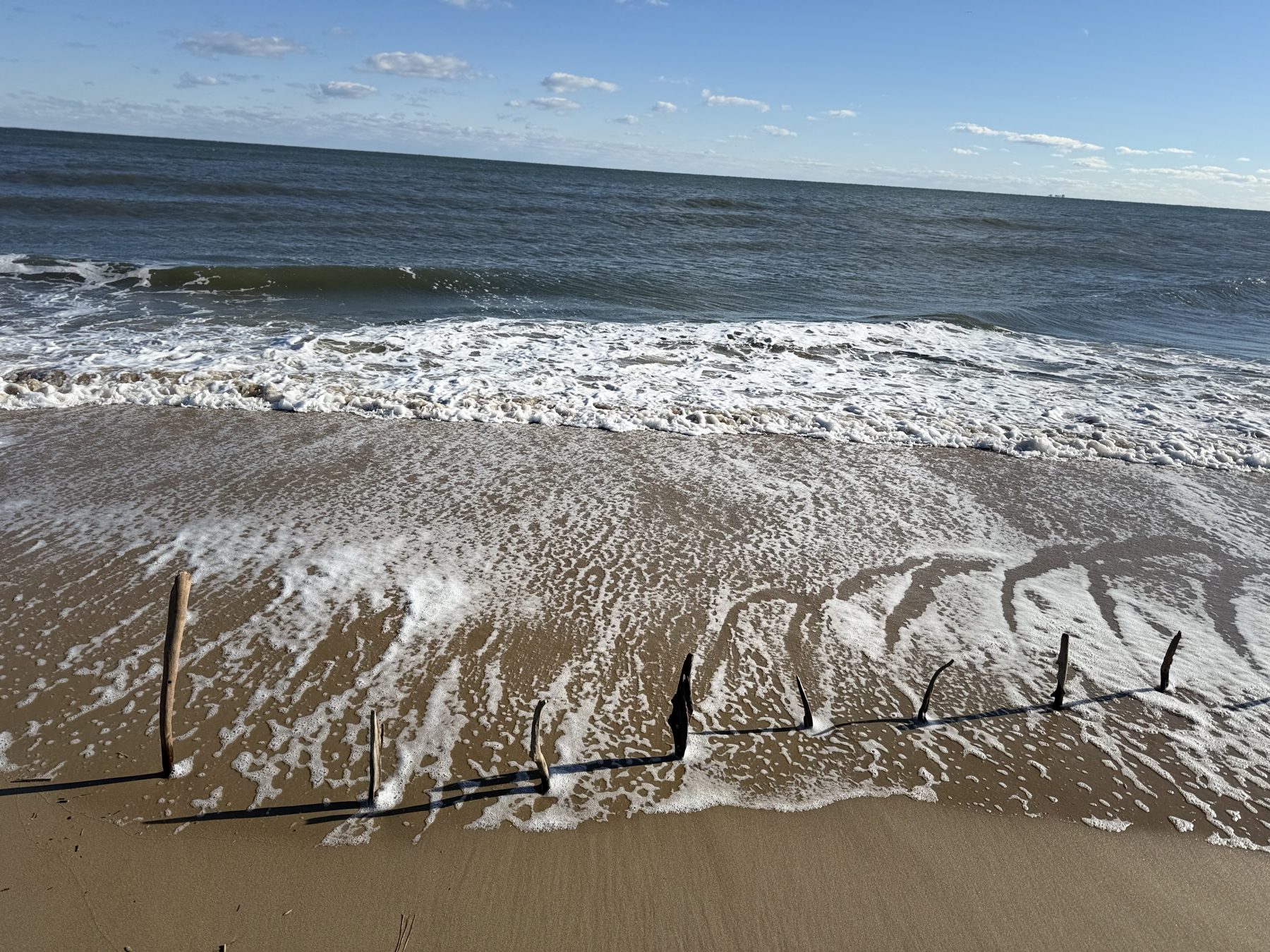 Wave foam crossing a horizontal line of sticks on the sand
