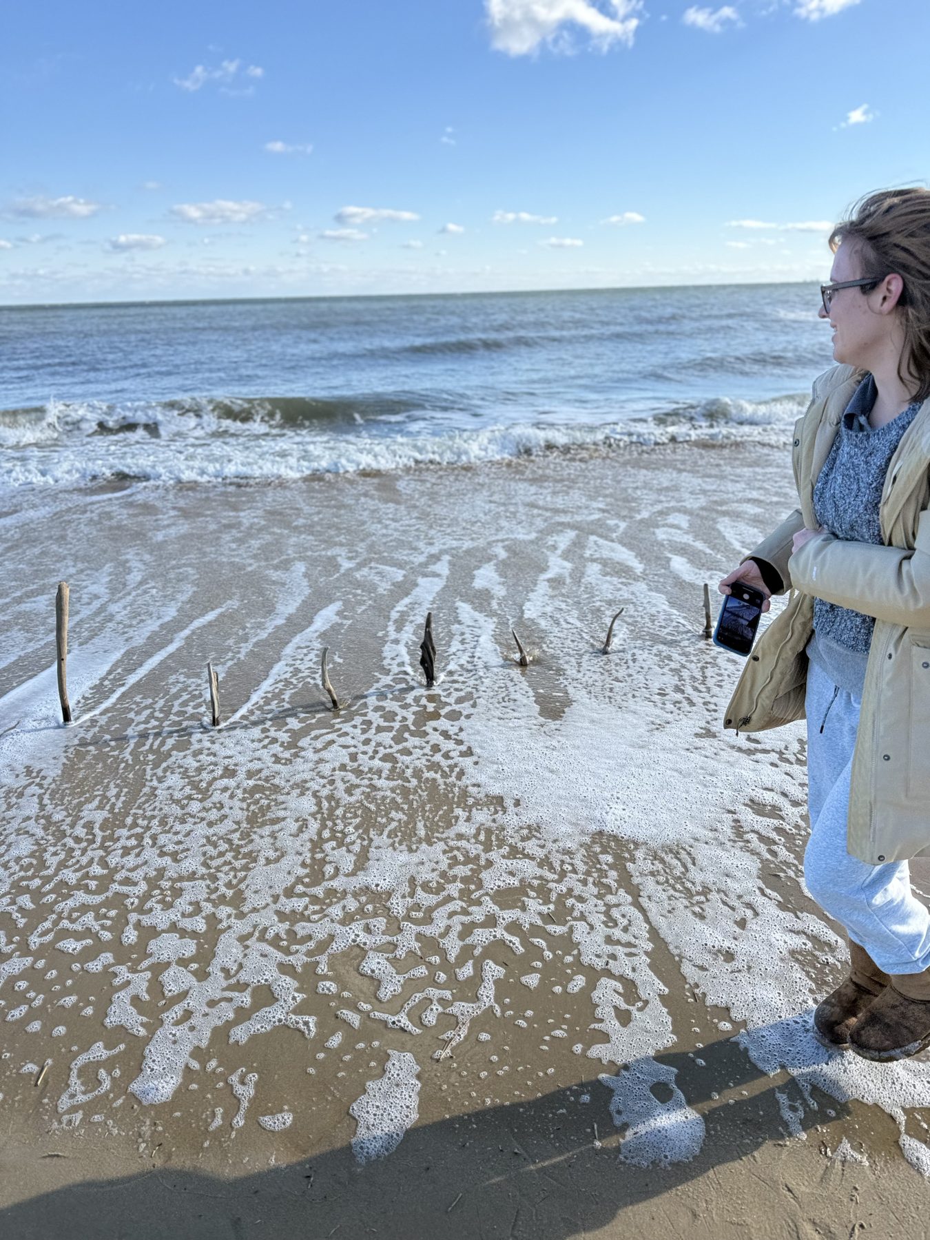 The artist standing in the shallow surf beside a row of sticks
