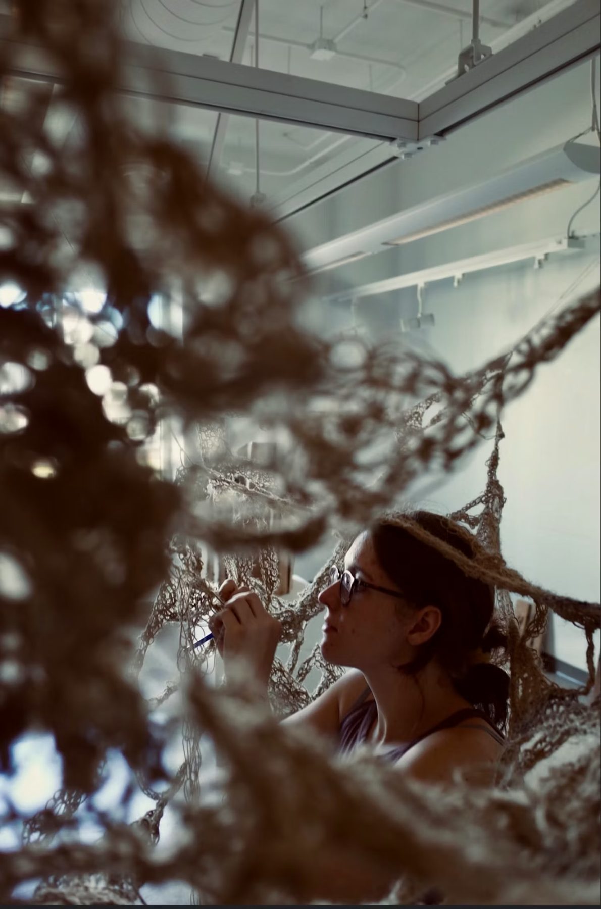 The artist seen through a large, loose suspended weaving